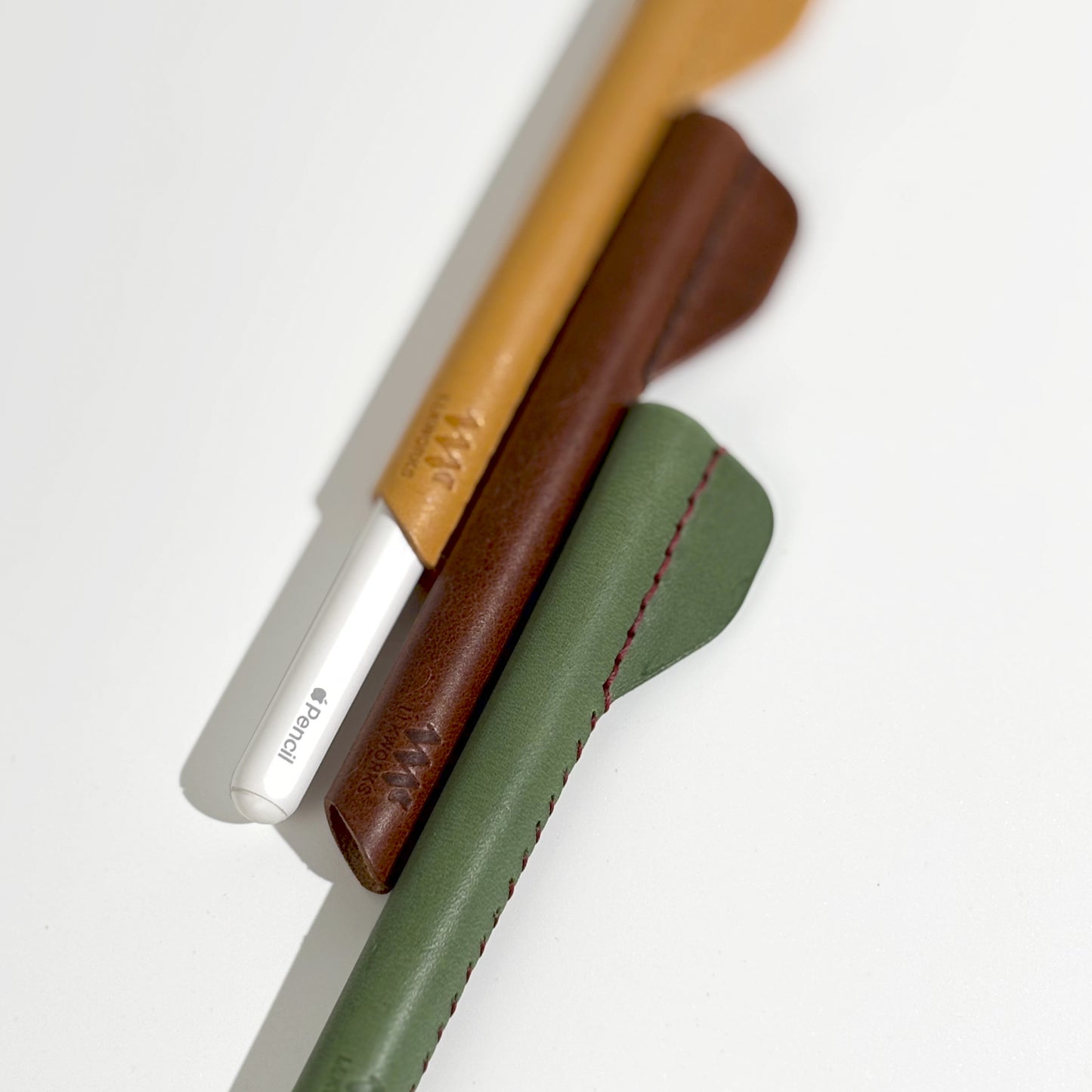 Close-up of a Apple Pencil alongside three artisan-crafted ergonomic leather grips in brown, yellow, and green, showcasing quality and design.