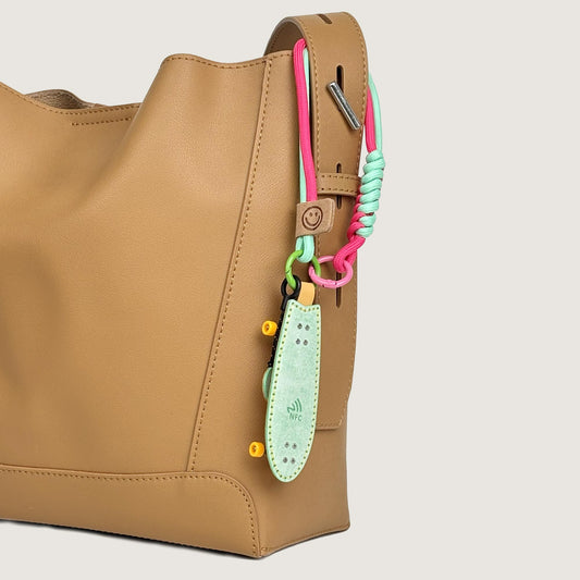 Waxy Veg-Tan leather fishtail skateboard bag charm hanging on a chic tan purse, perfect streetwear accessory for female skaters.