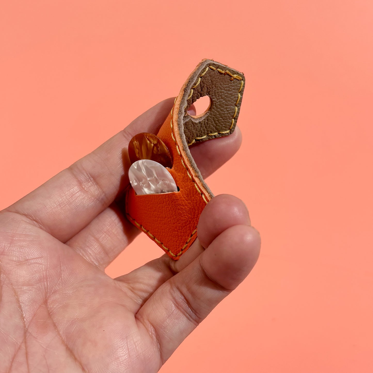 Orange hand-stitched leather guitar pick holder showing sheepskin texture