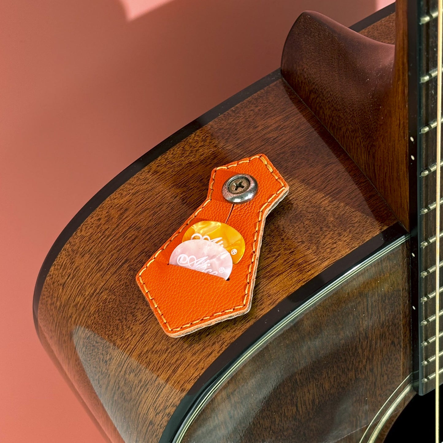 Orange handmade sheepskin leather guitar pick holder resting on a guitar