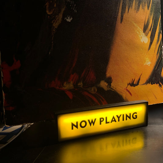 Illuminated "NOW PLAYING" LED sign on a vinyl record stand, creating a captivating display for current music.