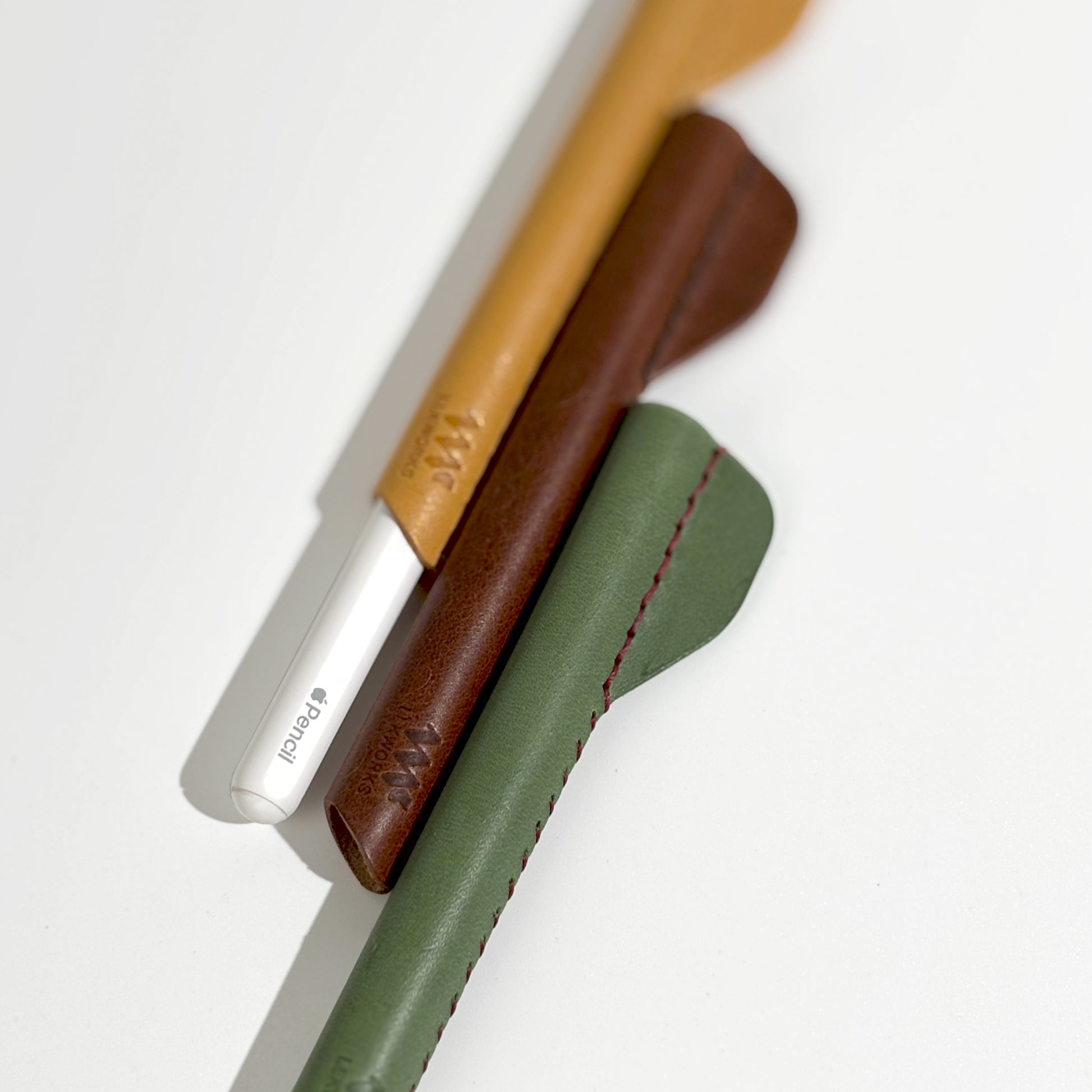 Close-up of a Apple Pencil alongside three artisan-crafted ergonomic leather grips in brown, yellow, and green, showcasing quality and design.