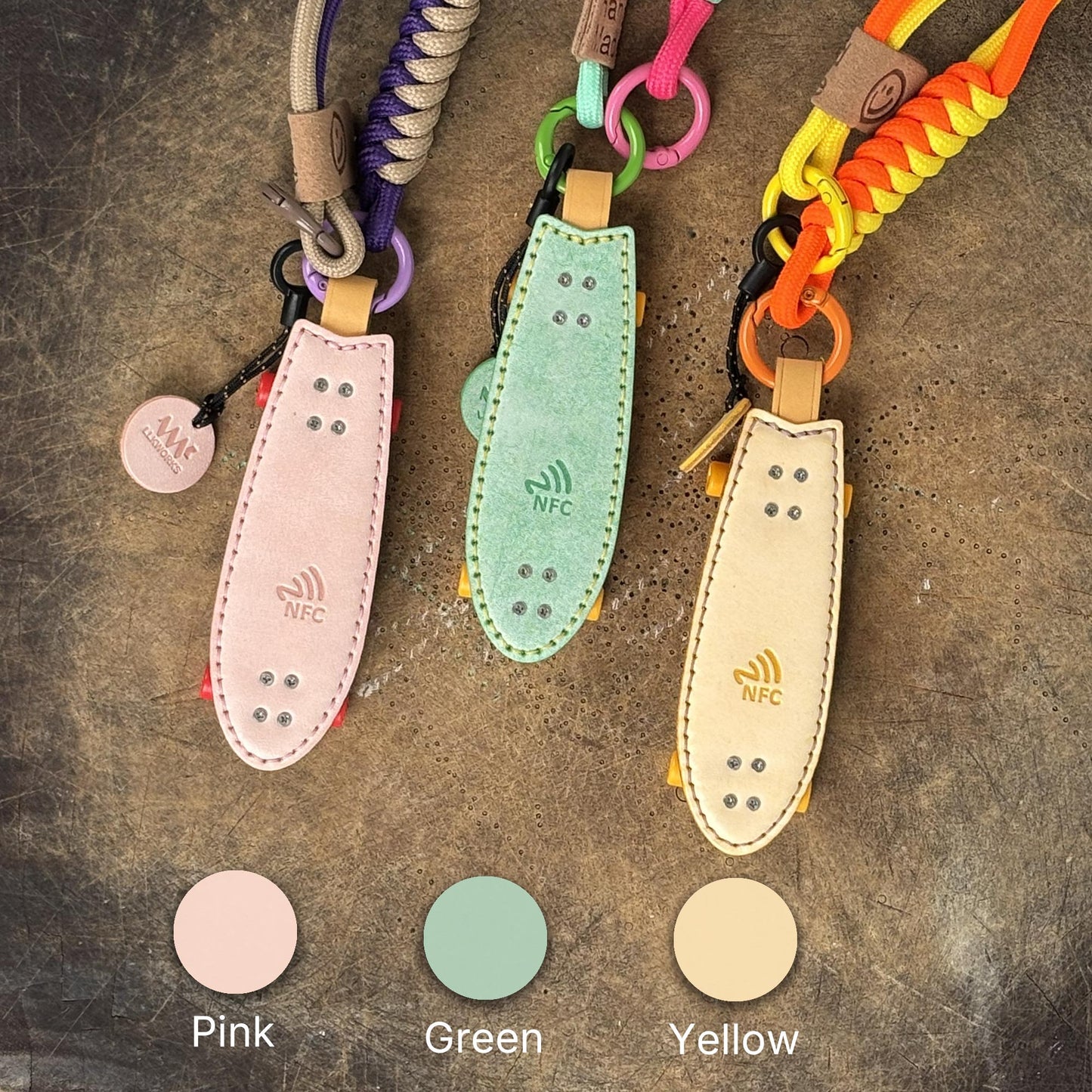 Three color variations of fishtail leather skateboard keyrings: Pink, Green, and Yellow.
