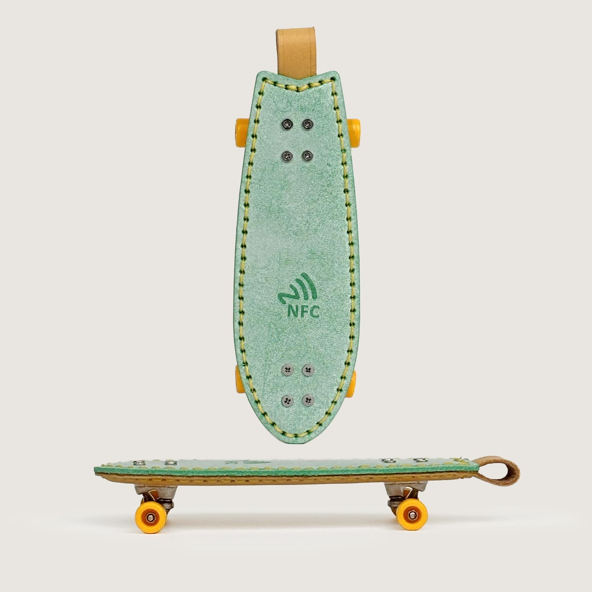 Green handmade leather fishtail skateboard keychain with built-in NFC tag, front view.