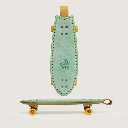 Green handmade leather fishtail skateboard keychain with built-in NFC tag, front view.