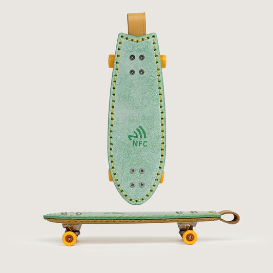 Green handmade leather fishtail skateboard keychain with built-in NFC tag, front view.