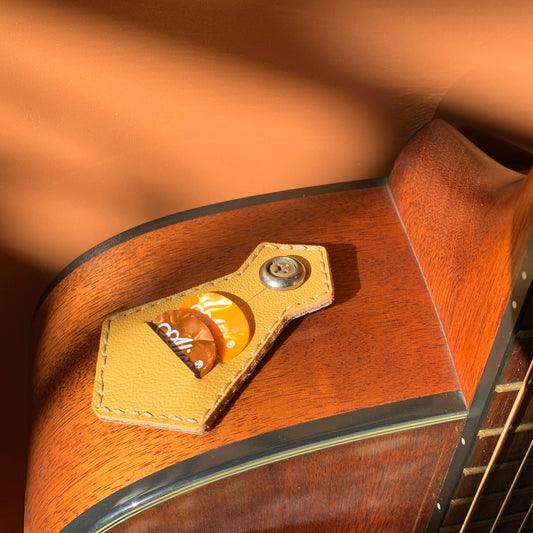 Yellow handmade sheepskin leather guitar pick holder with four guitar picks on an acoustic guitar, showcasing a compact hand-stitched 4-slot storage design for everyday playing.