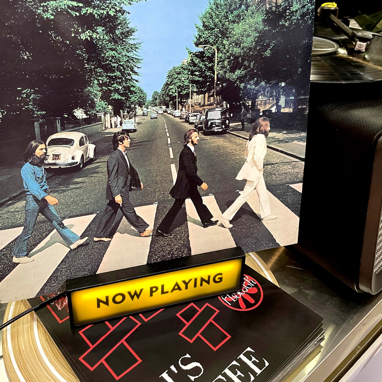 Now Playing" vinyl record display stand featuring The Beatles' "Abbey Road" album cover, with a vintage record player nearby, creating a musical ambiance.